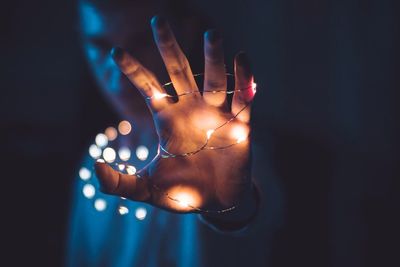 Close-up of man holding illuminated string light in dark at night