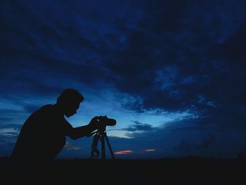 Silhouette photographer with camera on tripod against sky