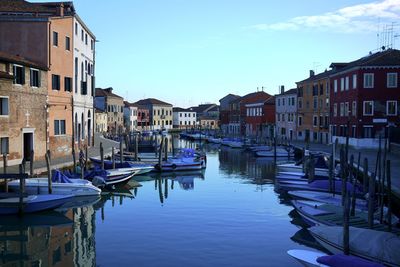 Boats moored in canal by buildings against sky in city