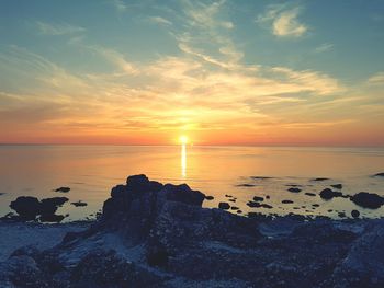 Scenic view of rocky shore and sea against sky during sunset