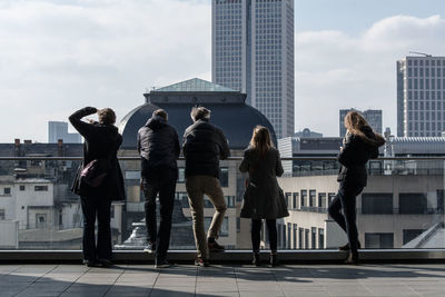 Rear view of people standing on building terrace in city during sunny day