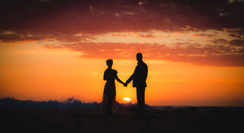 Silhouette couple standing at beach against sky during sunset