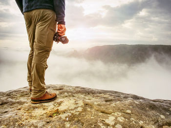 Photographer on mountain cliff looking into mist. hiker will take picture with small camera in hand