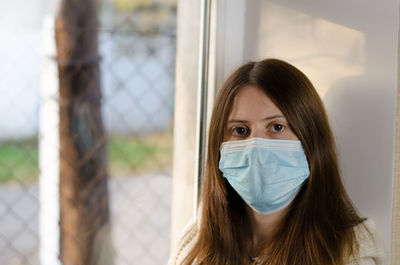 A young woman in a medical mask sits by the window. self-isolation concept. prevention covid 19