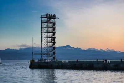 Crane by sea against sky during sunset