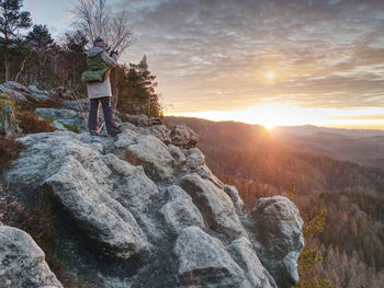 Man standing on rock against sky during sunset