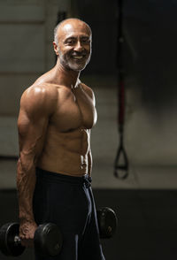 Shirtless man holding dumbbells in gym