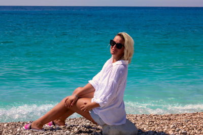 Young woman sitting on beach by sea