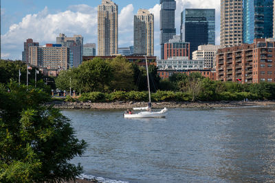 Sailboats sailing on river by buildings in city against sky