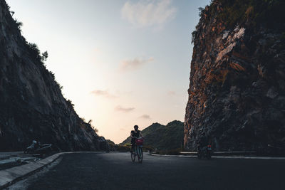 People riding bicycle on road against sky