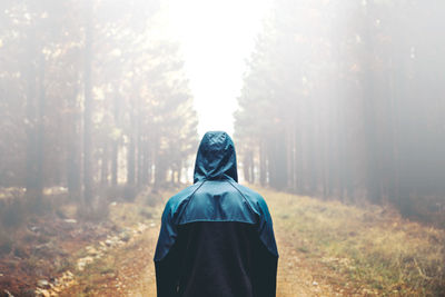 Rear view of person wearing raincoat amidst trees during rainy season