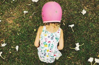 Rear view of girl wearing pink helmet while bending on grassy field