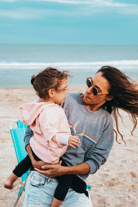 Woman carrying daughter while standing at beach