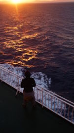 High angle view of man standing by railing and sea during sunrise