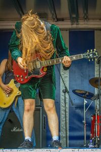 Full length of man with long hair playing guitar on stage