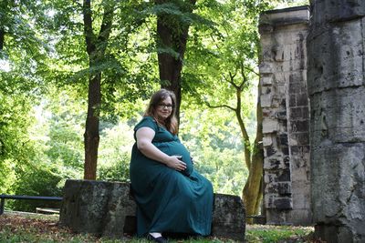 Portrait of pregnant woman sitting by tree
