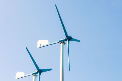 Low angle view of wind turbines against clear blue sky