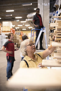 Female senior customer selecting plank while shopping at hardware store