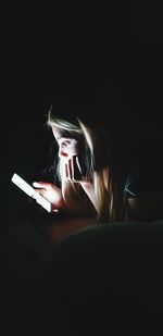 Teenage girl using phone on bed in darkroom