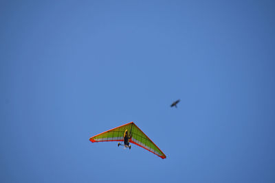 Low angle view of man hang gliding in clear blue sky