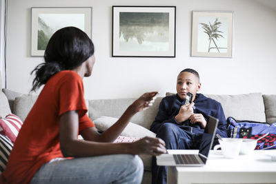 Boy showing mobile phone to mother with laptop and credit card in living room