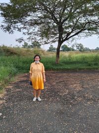 Asian woman wearing yellow dress take pictures under a large tree in the grandwisata