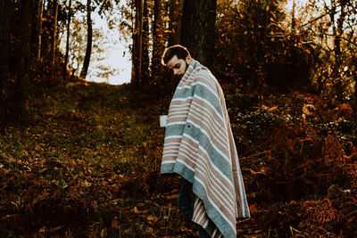 Man with shawl standing in forest during autumn