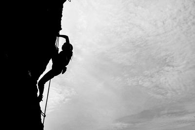 Low angle view of silhouette man against sky rock climbing