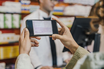 Hand of customer using smart phone for prescription in chemist store