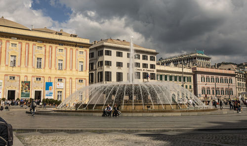 People in front of building against cloudy sky