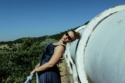 Portrait of young woman standing by pipes against clear blue sky