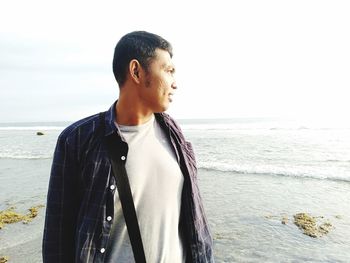 Young man looking at sea shore against sky