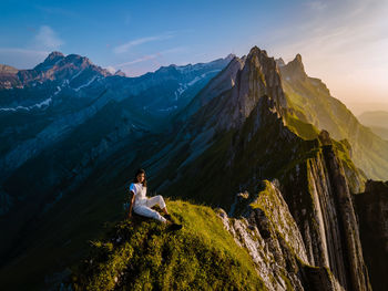 Man sitting on rock by mountain against sky