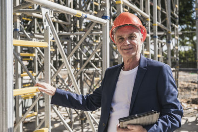 Smiling architect with tablet pc standing by scaffolding