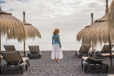 Rear view of woman standing at beach against sky