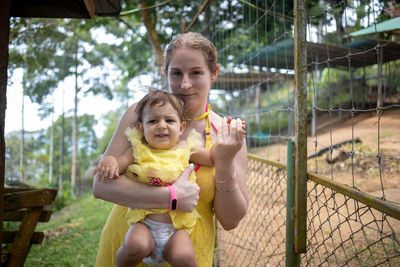 Portrait of mother and daughter standing by chainlink fence