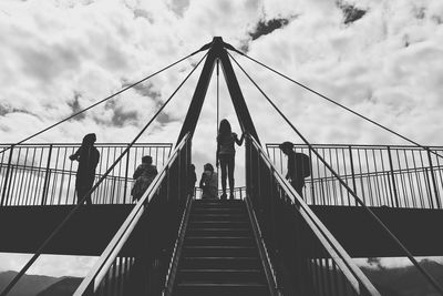 Low angle view of people walking on footbridge against sky