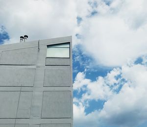 Low angle view of bird perching on building against sky