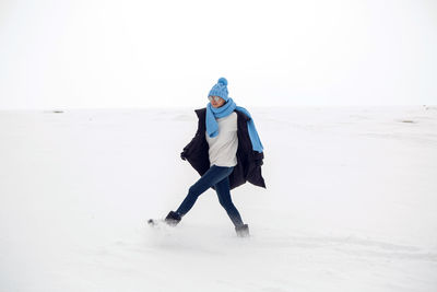 Girl running in a snowy field in a jacket and sunglasses