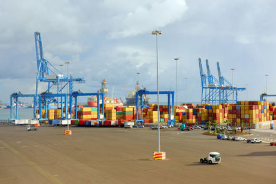 Cargo containers at commercial dock against cloudy sky