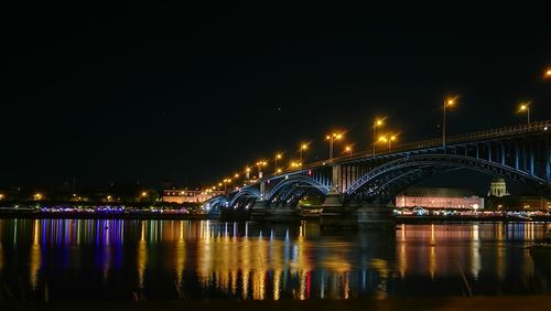 Illuminated bridge over river against sky at night