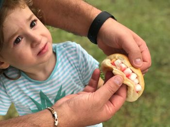 Cropped hands of father holding food with daughter on field