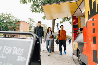 Full length of friends walking on street by food truck in city