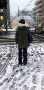 Rear view of woman walking on snow in city