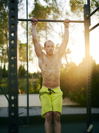 Shirtless fit young man working out in a cage at outdoors gym