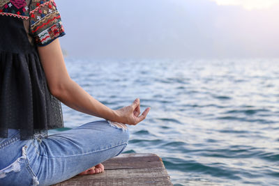 Low section woman sitting in lotus position on pier over sea