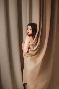 Portrait of young woman standing against red curtain