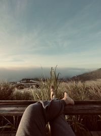 Low section of man sitting on field against sky during sunset