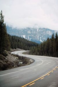 Empty winding road surrounded by trees and mountains