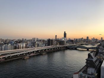 Bridge over river by buildings in city against sky during sunset